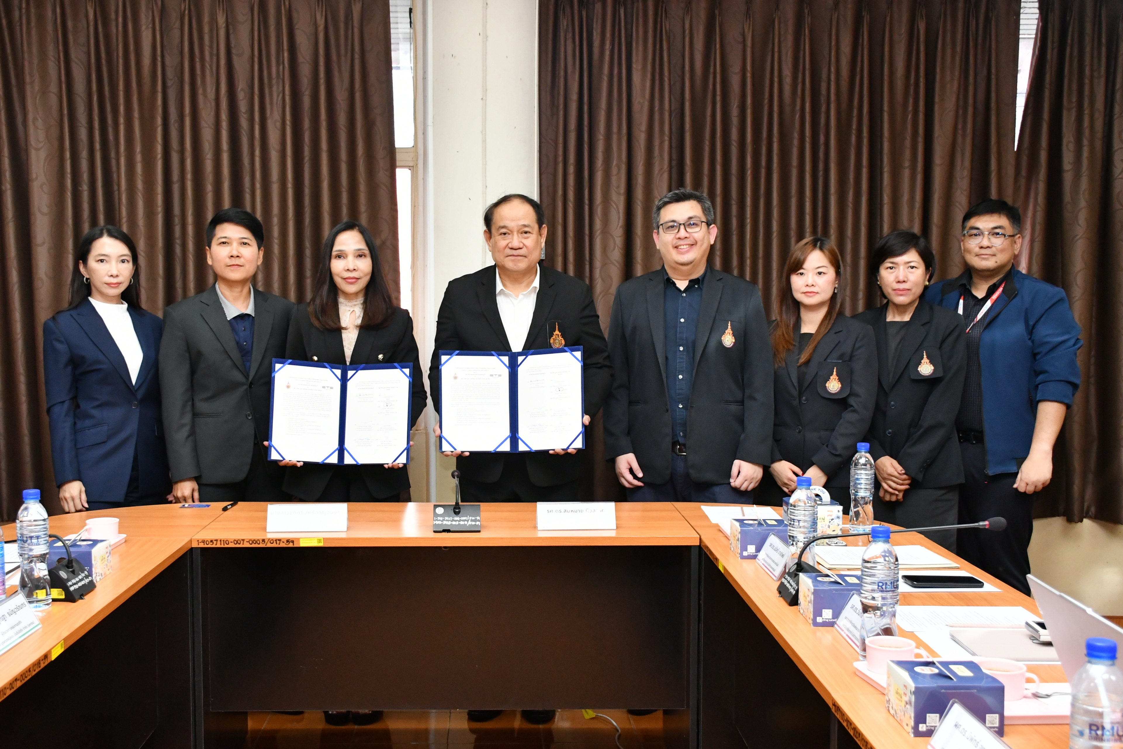 กลุ่มผู้บริหารและตัวแทนจากสององค์กรยืนเรียงแถวร่วมถ่ายภาพเป็นที่ระลึกในพิธีลงนามบันทึกข้อความตกลงความร่วมมือ (MOU) โดยมีผู้แทนถือแฟ้มสัญญาเปิดโชว์อยู่ด้านหน้า